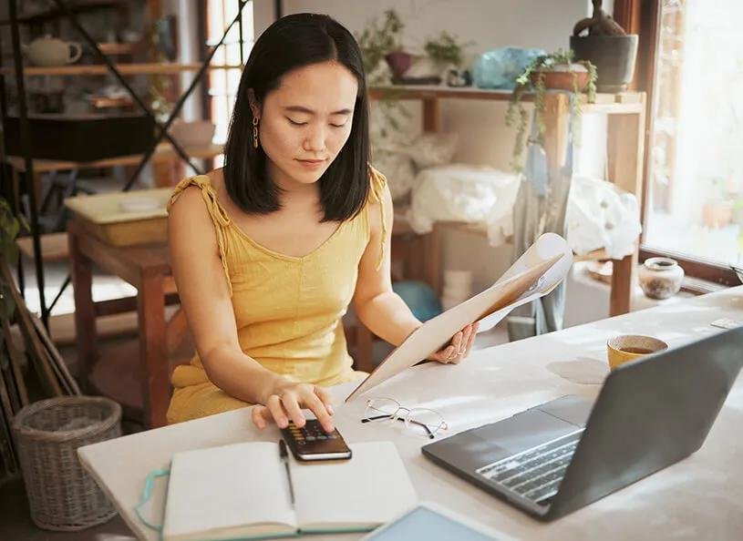 Small business owner reviewing finances at a desk with a calculator, notebook, and laptop